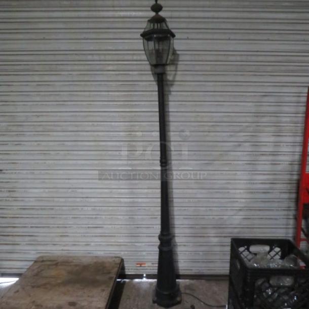Antique-style electric street light, tall black metal pole with glass lantern top, minimal wear, vintage aesthetic.