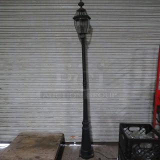 Antique-style electric street light, tall black metal pole with glass lantern top, minimal wear, vintage aesthetic.