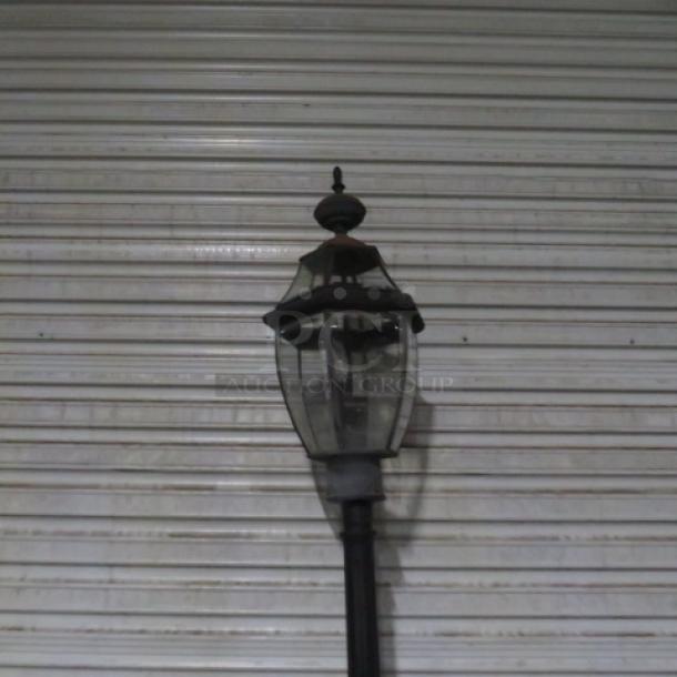 Vintage-style electric street light with glass panels and ornate black metal frame. Slight wear visible, mounted on a pole.