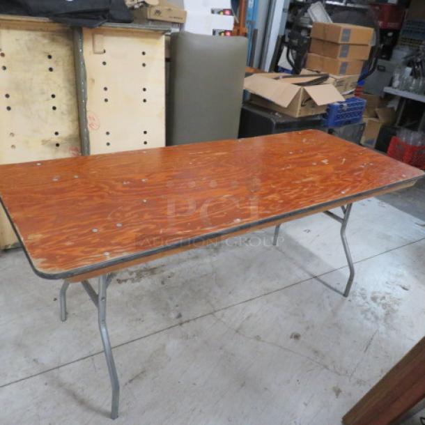 Wooden folding table with metal legs, 72x30x30 inches. Surface shows minor wear, suitable for events or temporary setups.