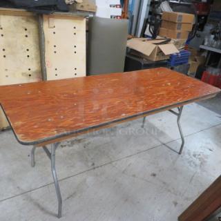 Wooden folding table with metal legs, 72x30x30 inches. Surface shows minor wear, suitable for events or temporary setups.