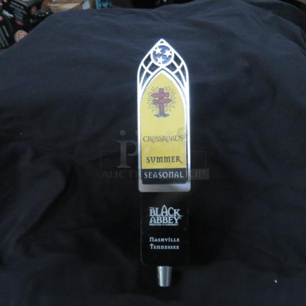 Beer tap handle with "Crossroads Summer Seasonal" label, Black Abbey Brewing logo, and gothic arch design.