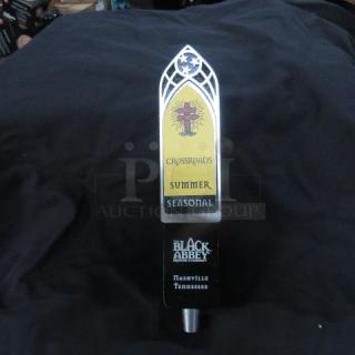 Beer tap handle with "Crossroads Summer Seasonal" label, Black Abbey Brewing logo, and gothic arch design.