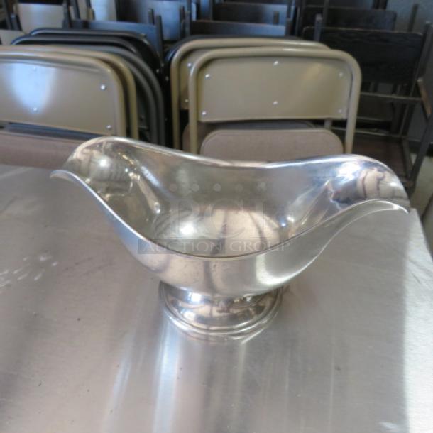 Stainless steel gravy boat with sculpted edges, polished finish, excellent condition, on a shiny metal surface.