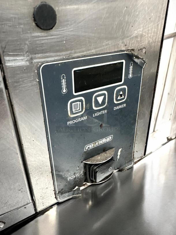 Roundup conveyor toaster control panel with temperature settings, power switch, and brand logo. Stainless steel surface.