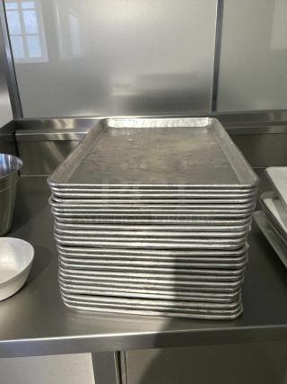 A stack of 1/2" size bakery sheet pans in great condition, shown on a stainless steel surface.