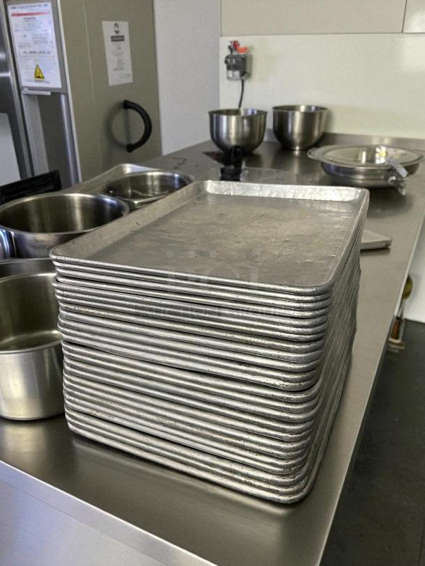 Stack of 1/2" size bakery sheet pans in great condition, on a stainless steel counter, surrounded by mixing bowls.