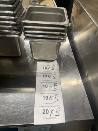 Commercial stainless steel hotel steamtable pans stacked on metal surface. Tags show multiples of 5 available for auction.