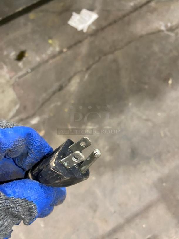 Close-up of a power plug handled by a person wearing blue gloves, related to Haier commercial chest freezer model HE71CL53NW.