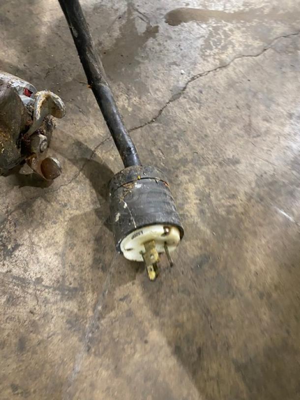 A damaged black electrical plug with visible prongs and wear, lying on a concrete floor.