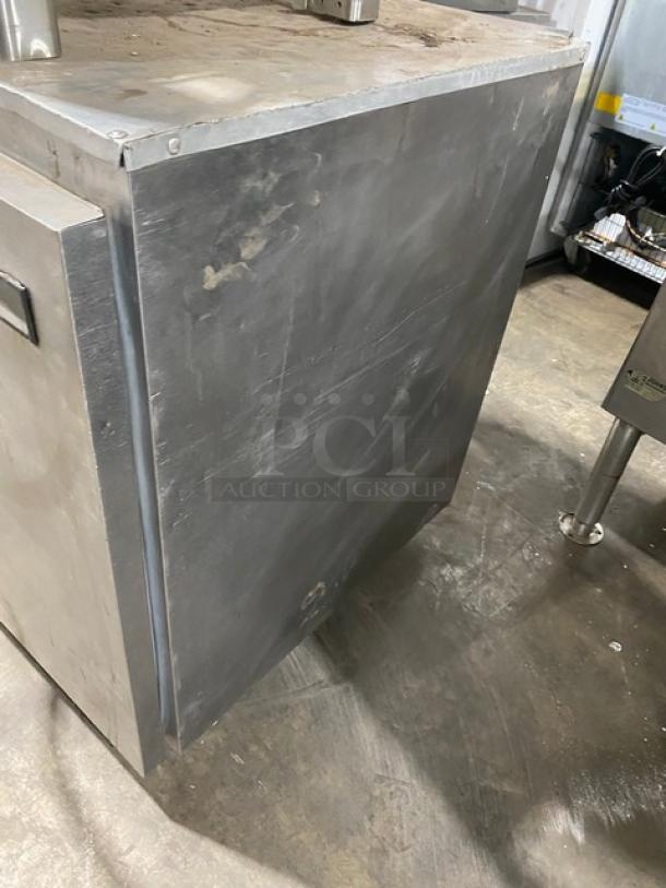Commercial stainless steel undercounter refrigerator with single solid door, poly-coated wire rack, and casters. Shows wear.