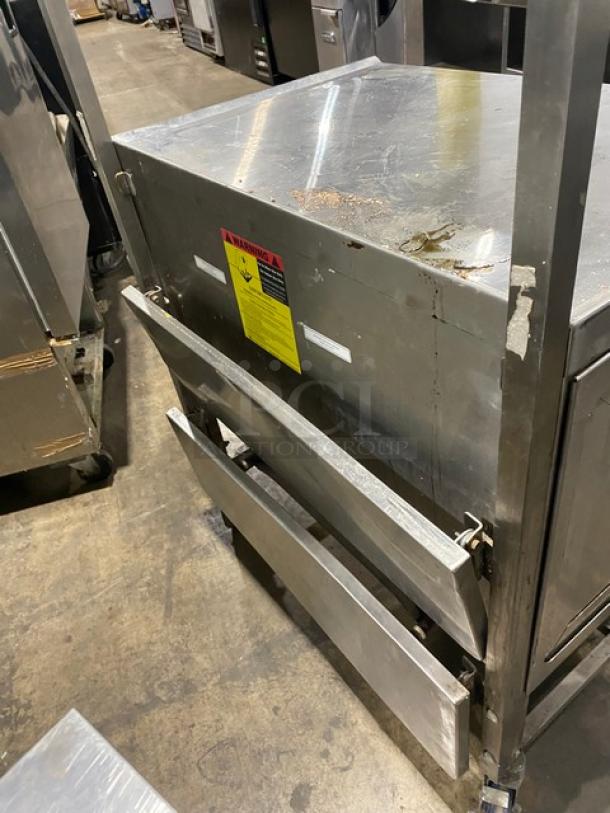 Stainless steel worktop/prep table with enclosed base, double foldable shelf, and casters. Some wear visible. Warning label attached.