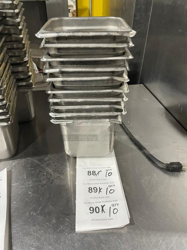 Stainless steel hotel pans stacked on a metal surface, featuring durable construction and a sign indicating auction bids.