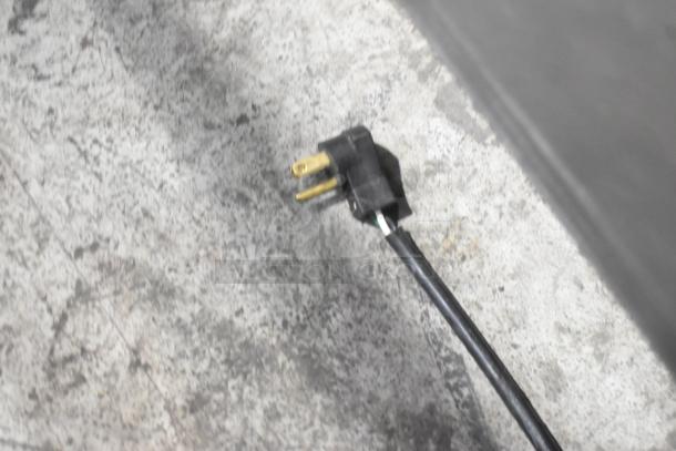 Black power cord with a three-prong plug on a gray, textured surface.