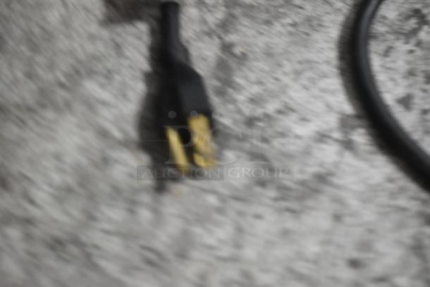Blurry image of a power plug on a gray surface, context suggests it belongs to an Oliver 777 Bread Loaf Slicer.