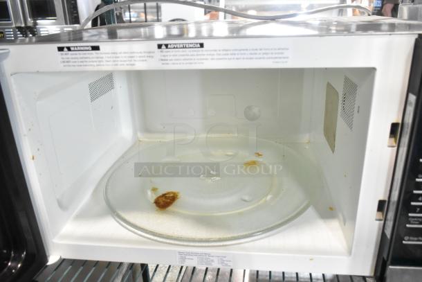 Stainless steel countertop microwave oven, used with visible stains, 120 volts, 1 phase. Warning label on door.