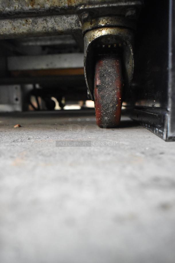 Underneath view of a Leader stainless steel commercial cooler, showing a worn caster wheel. 4 drawers, 115 volts, 1 phase.