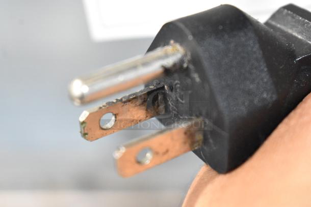 Close-up of a three-prong electrical plug with slight wear, showing the prongs and black plastic casing.