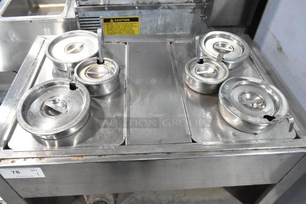 Stainless steel commercial 2-well steam table with lids and cylindrical drop-in bins, used condition; caution label visible.