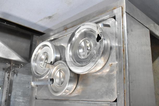 Stainless steel commercial 2 well steam table with cylindrical drop-in bins, showing lidded containers and slight wear.