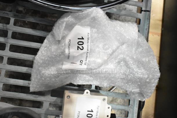 New scratch and dent faucet wrapped in bubble wrap on metal shelf, auction tag '102' visible.