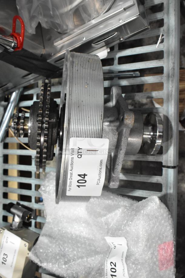 Brand new scratch and dent metal gear with chain assembly, marked "104" with auction details on label, displayed on metal shelf.