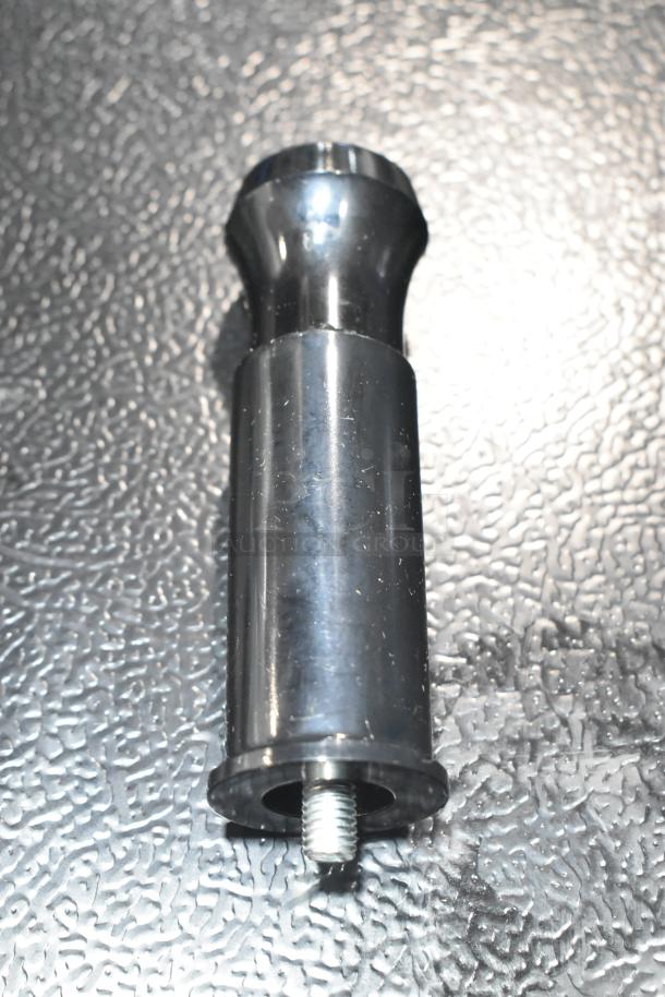 Metal component with a threaded end, possibly a part of a commercial machine, placed on a textured surface.