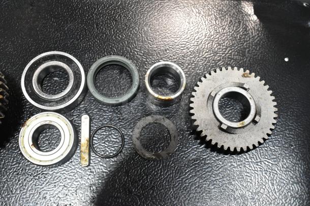 BRAND NEW SCRATCH AND DENT metal gear set with bearings and seals, showing minor oxidation, laid out on black surface.