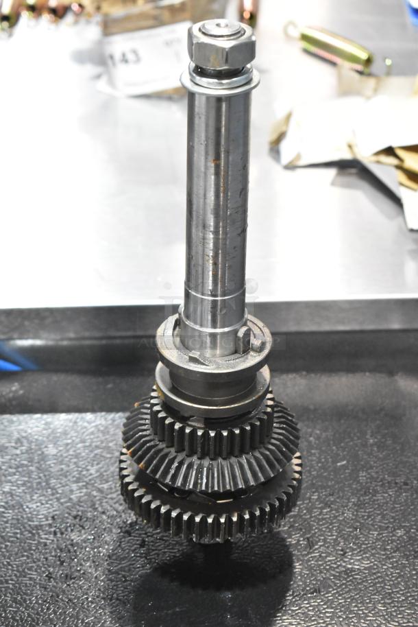 Brand new metal gear with minor scratches and dents. Tall central shaft, intricate gear teeth. Appears unused.