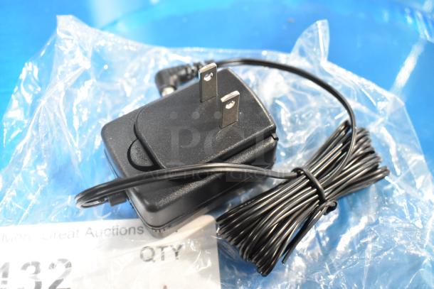 Black power adapter and cord on clear plastic wrap with auction label showing lot number 132.