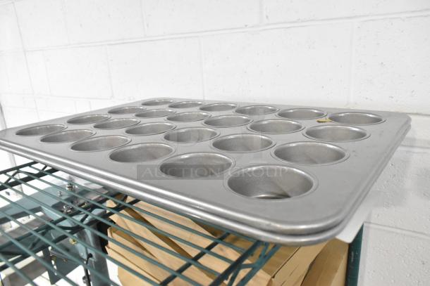 Metal 24-cup muffin baking pan, brand new with minor scratches and dents, shown on a wire shelf.