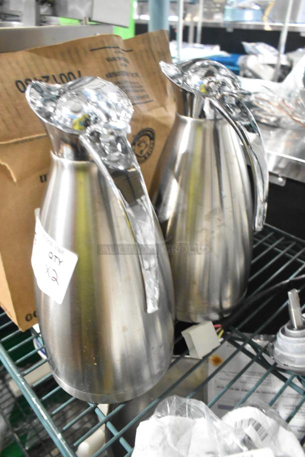 Two brand new metal pitchers with slight scratch and dent. Includes quantity label showing "x2." Sleek, polished finish.