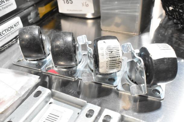 Lot with 4 brand new commercial casters, metal base, black wheels, minor scratches, visible barcodes on wheels.