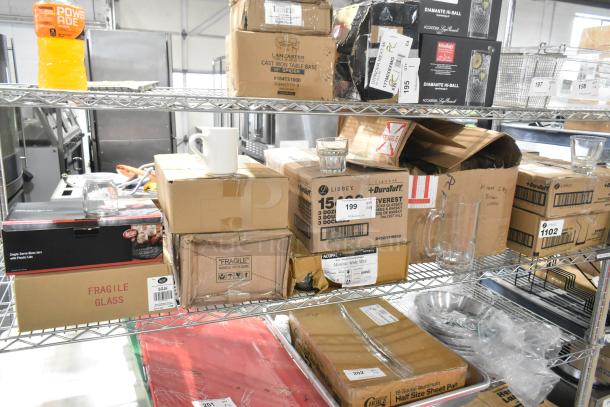 Auction items including glassware and mugs on storage shelves; boxes showing labels like Tablecraft SGJ6, Acopa, Libbey, indicating new items.