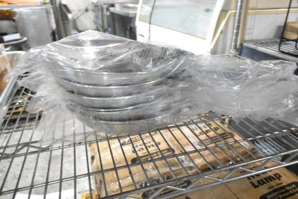 Stack of 6 Choice 407FRYPAN 10" aluminum fry pans, brand new, wrapped in plastic with slight cosmetic dents, on a metal shelf.