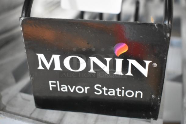 Black metal 4-tier stand with "Monin Flavor Station" label, scratch and dent condition, brand new.