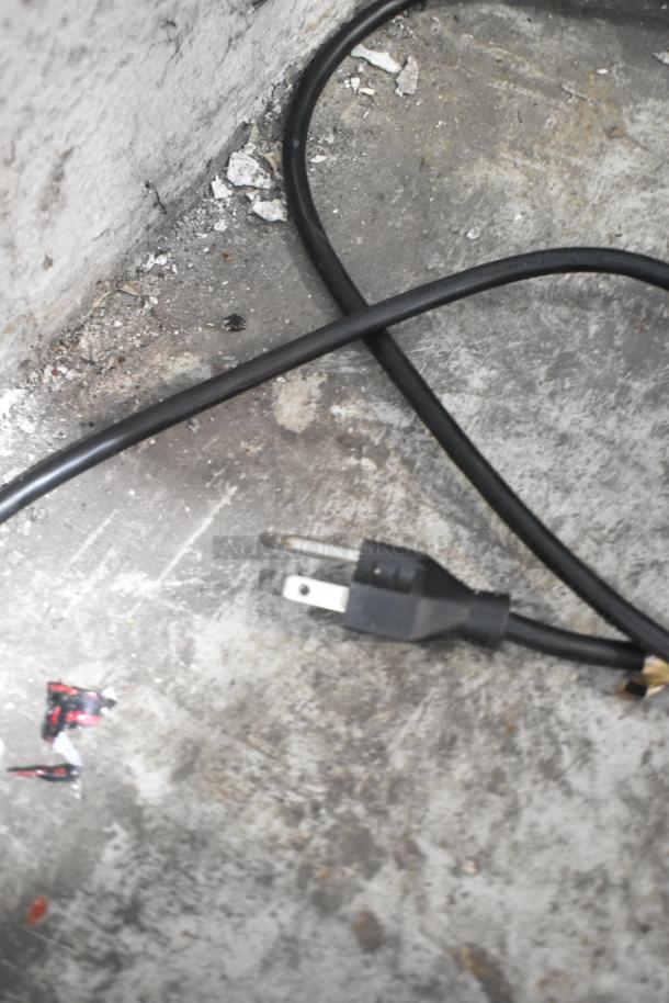 Alt text: Close-up of a damaged electrical plug on a concrete floor.