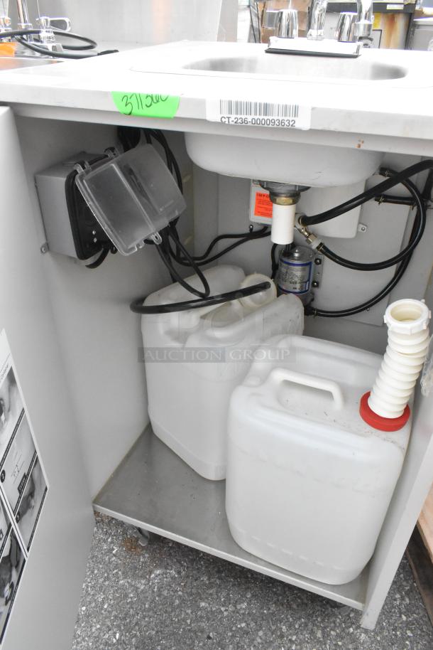 Stainless steel single bay portable sink on commercial casters, includes attached hoses and storage containers below.