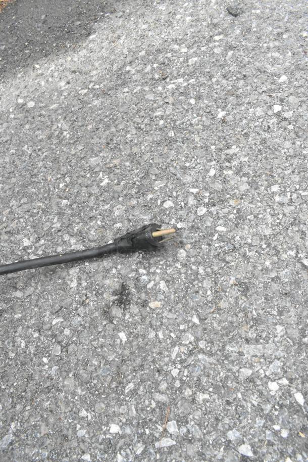 A damaged power cord on rough asphalt.
