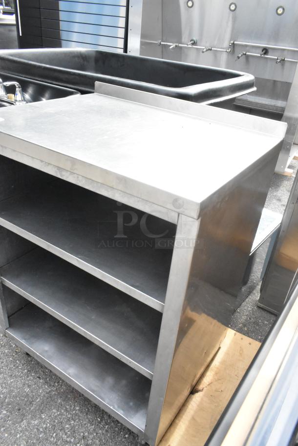 Stainless steel counter with three under shelves, shows minimal wear, ideal for kitchen or industrial use.