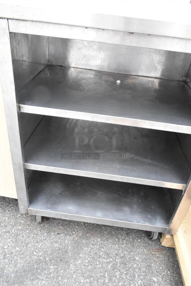 Stainless steel counter with three under shelves, industrial-grade, minor wear, suitable for commercial kitchens.