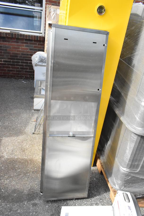 Stainless steel wall mount trash and towel dispenser, brand new with minor scratches, standing next to yellow structure.