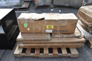 Cardboard boxes labeled "Spartech" with visible damage, containing new scratch and dent items, placed on a wooden pallet.