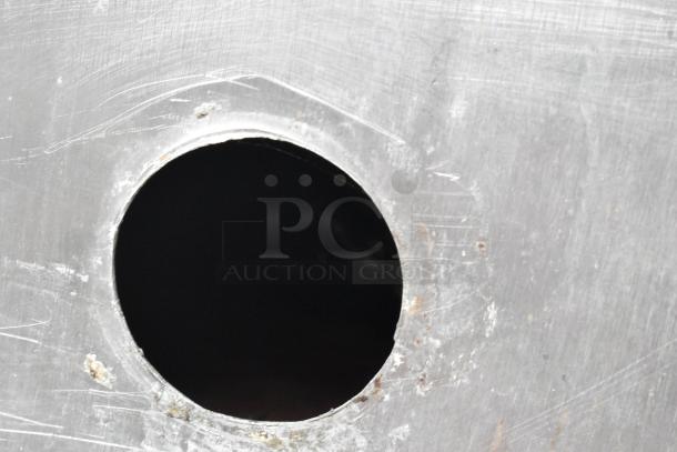 Stainless steel braising pan surface with a round cut-out, showing wear and scratches.