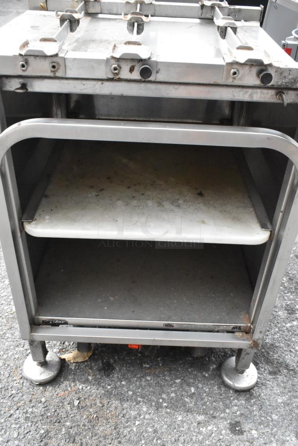 M&E metal equipment stand, stainless steel with visible wear, dual shelves, sturdy legs. Ideal for industrial use.