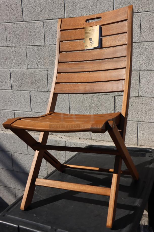 Brand new Outdoor Interiors Eucalyptus folding armless chair, model 10050. Tag visible, indicating hardwood construction.