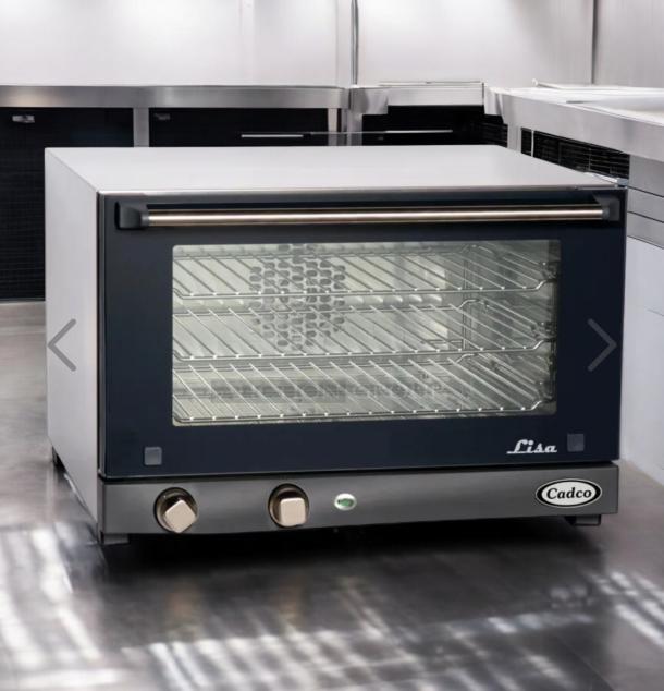 Brand new Cadco OV-013 half-size convection oven, stainless steel, unopened box, 120V. Model label and controls visible.