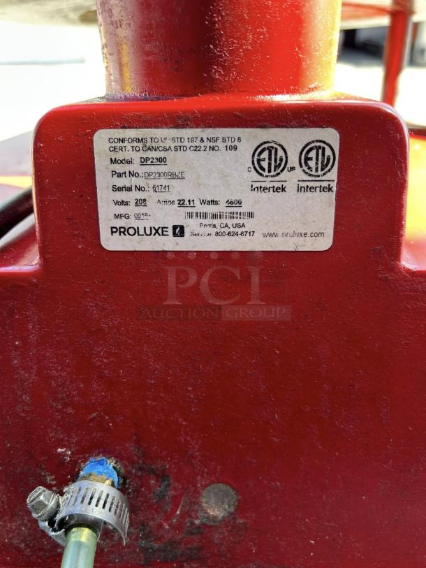 Proluxe DP2300 pizza press label, showing model details, certifications, and contact info. Red surface and attached tubing visible.