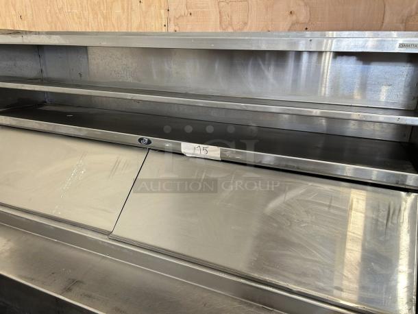 Stainless steel countertop display unit with shelving, minor wear, sticker labeled "125" on the front.