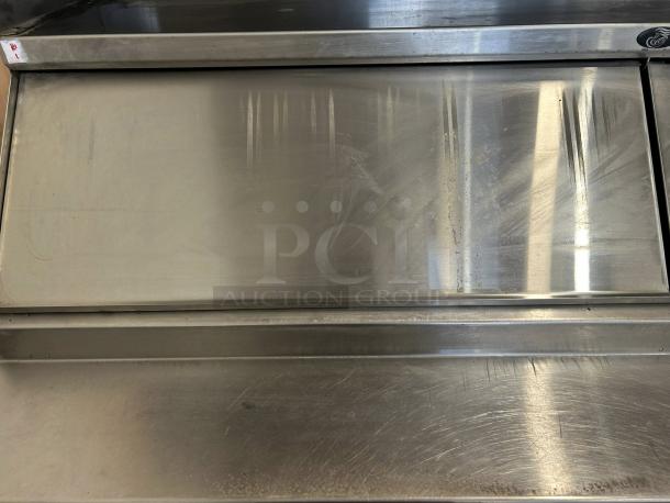 Stainless steel kitchen appliance with sliding top, showing visible wear and surface scratches. No labels or markings noted.